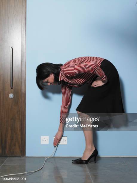 businesswoman bending to reach plug socket - vornüber beugen stock-fotos und bilder