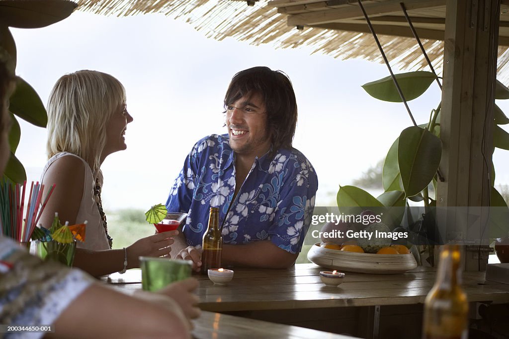 Young couple sitting at beach bar, smiling at each other