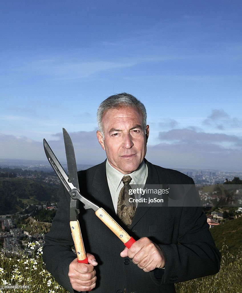 Mature businessman holding hedge shears, portrait