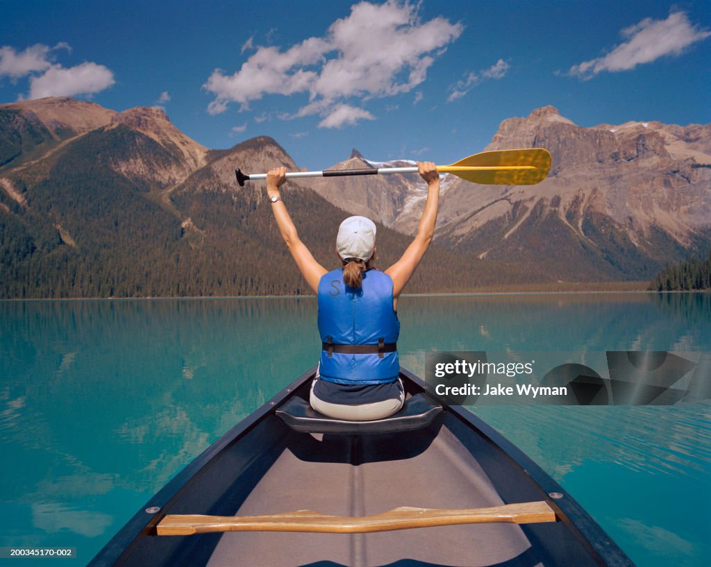Mature woman in canoe, holding oar in air, rear view