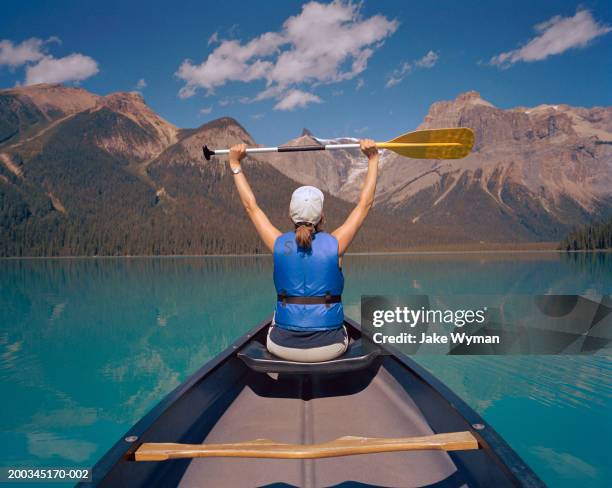 mature woman in canoe, holding oar in air, rear view - life vest stock pictures, royalty-free photos & images