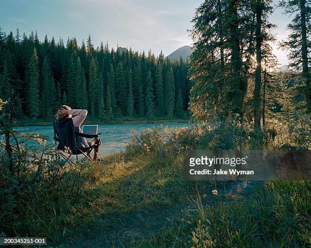 mature woman on chair with laptop near lake, side view - telecommuting fotografías e imágenes de stock