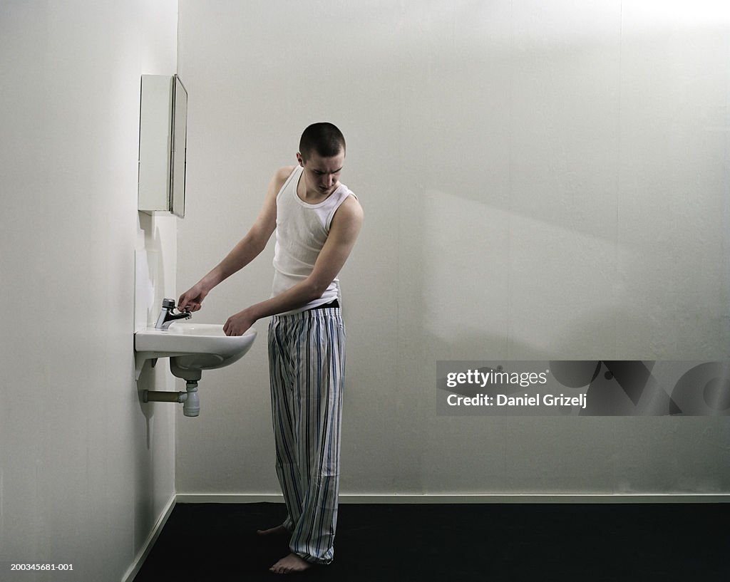 Young man holding tap in sink, looking at floor