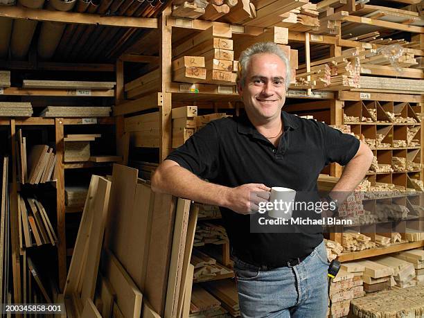 man holding mug by planks of wood on shelves, smiling, portrait - wood worker posing ストックフォトと画像