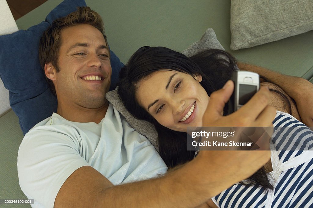 Young couple lying on sofa, taking photo with mobile, elevated view