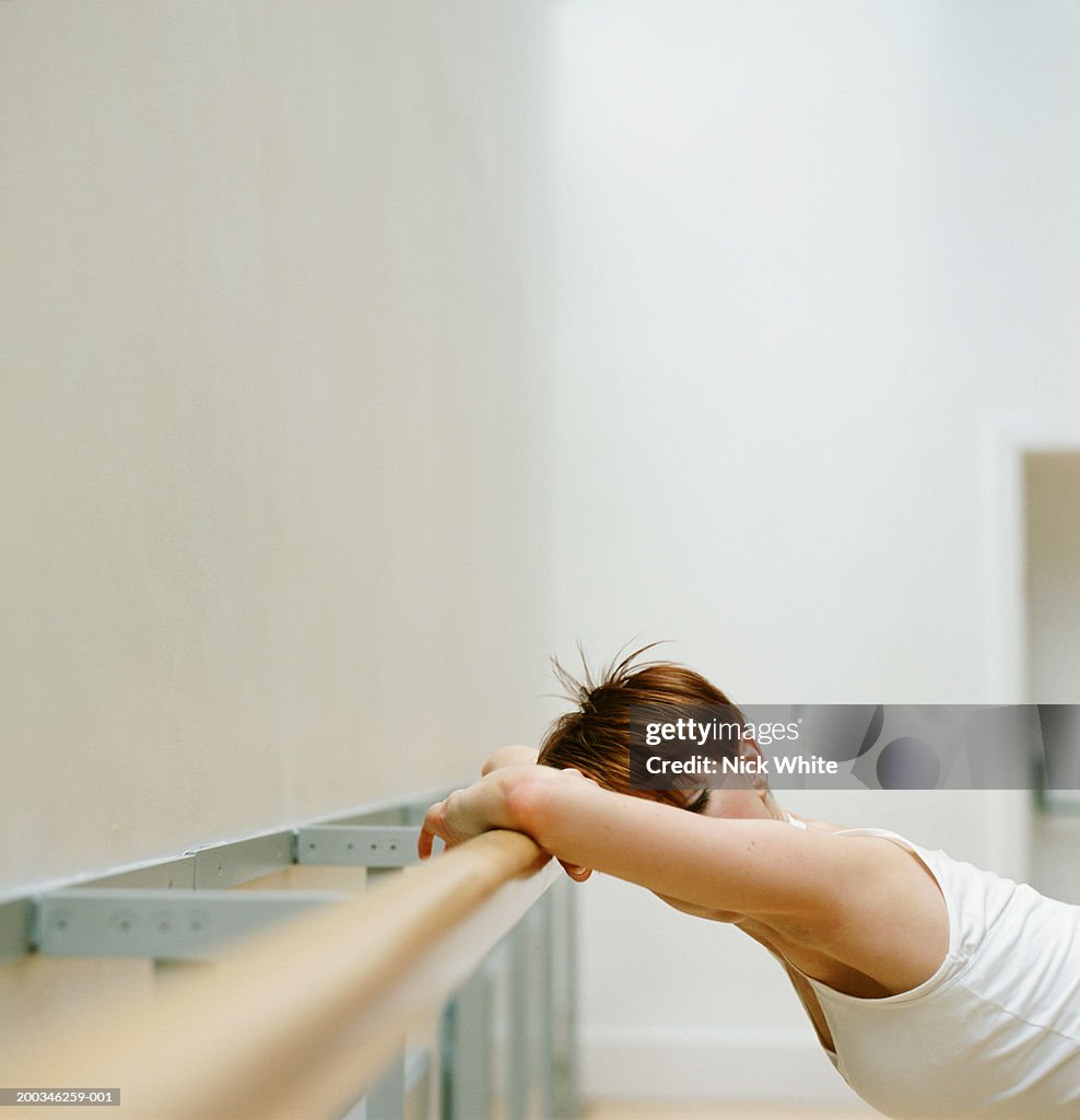 Young woman leaning against rail in dance studio, stretching