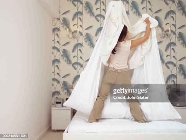 young woman standing on bed changing duvet cover, rear view - duvet stock pictures, royalty-free photos & images