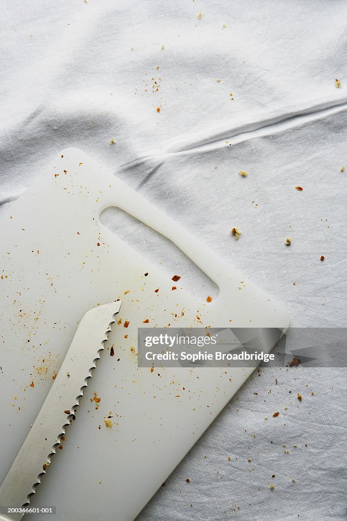 Breadknife on cutting board, crumbs on table cloth and board, close-up