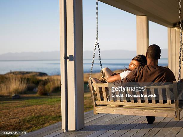 woman and mature man sitting on swing chair on porch - back porch stockfoto's en -beelden