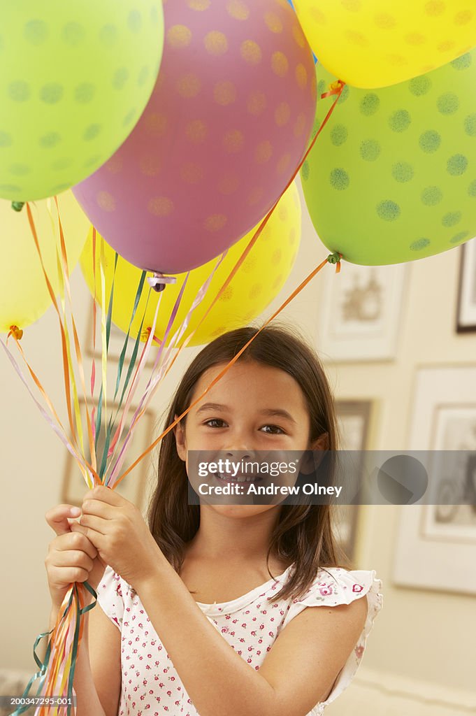 Girl (5-7) holding bunch of helium balloons, smiling, portrait