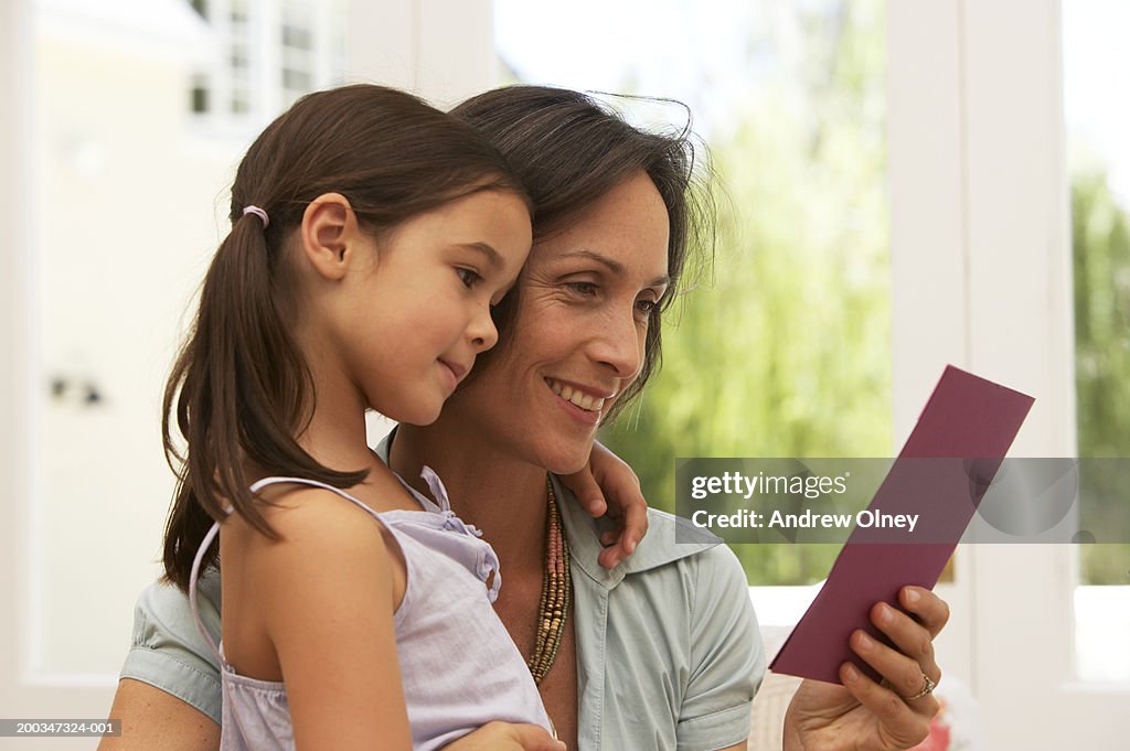 Mother and daughter (5-7) embracing, woman holding card