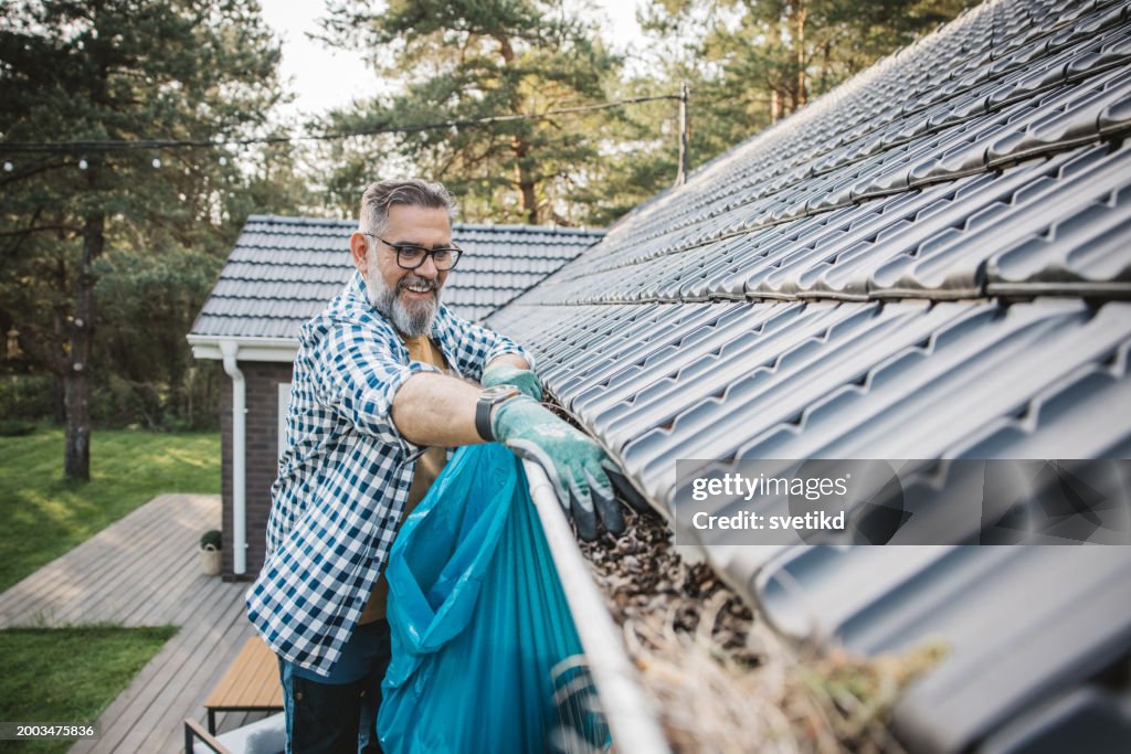 家の側溝から葉を掃除する男