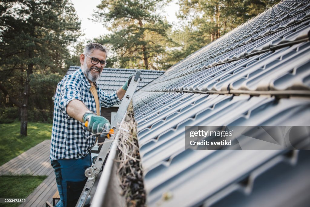 Man cleaning leaves from guttering of house