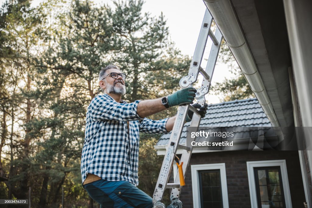 Man cleaning leaves from guttering of house