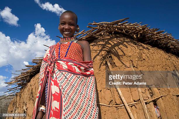 maasai girl (11-13) standing outside mud hut, smiling, portrait - masai mara national reserve stock-fotos und bilder