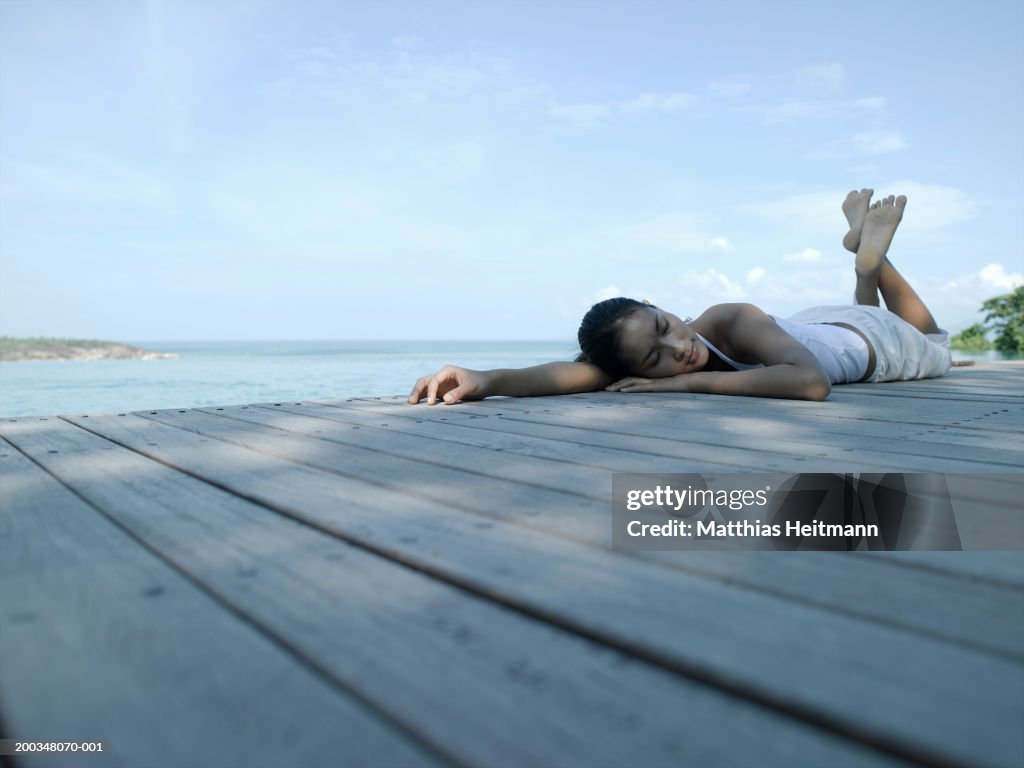 Woman lying on boardwalk, eyes closed, ground view