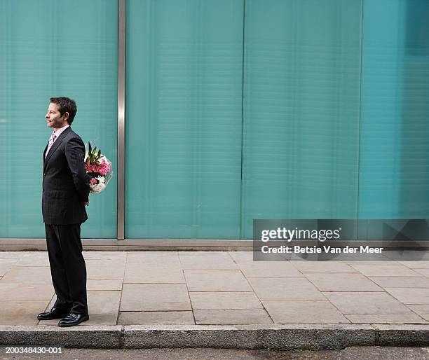 businessman standing on pavement, bunch of flowers behind back - hands behind back stockfoto's en -beelden