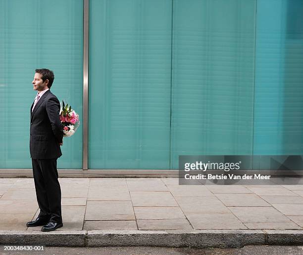 businessman standing on pavement, bunch of flowers behind back - mãos atrás das costas - fotografias e filmes do acervo