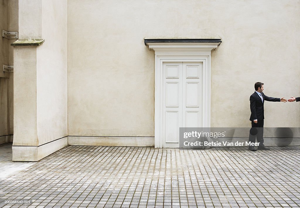 Businessman about to shake man's hand outdoors, side view