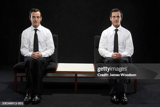 twin brothers sitting on chairs, wearing suits - dubbel stockfoto's en -beelden