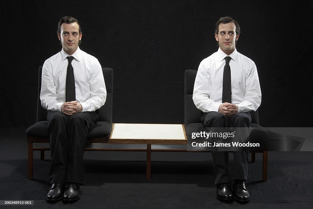 Twin brothers sitting on chairs, wearing suits