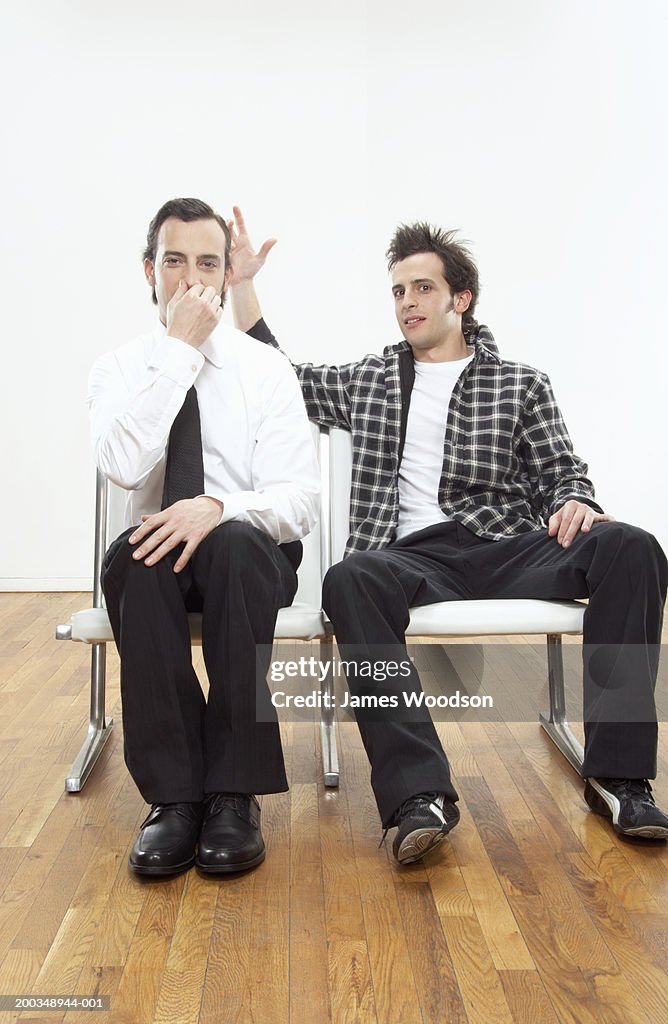 Twin brothers sitting side by side, one wearing suit, portrait