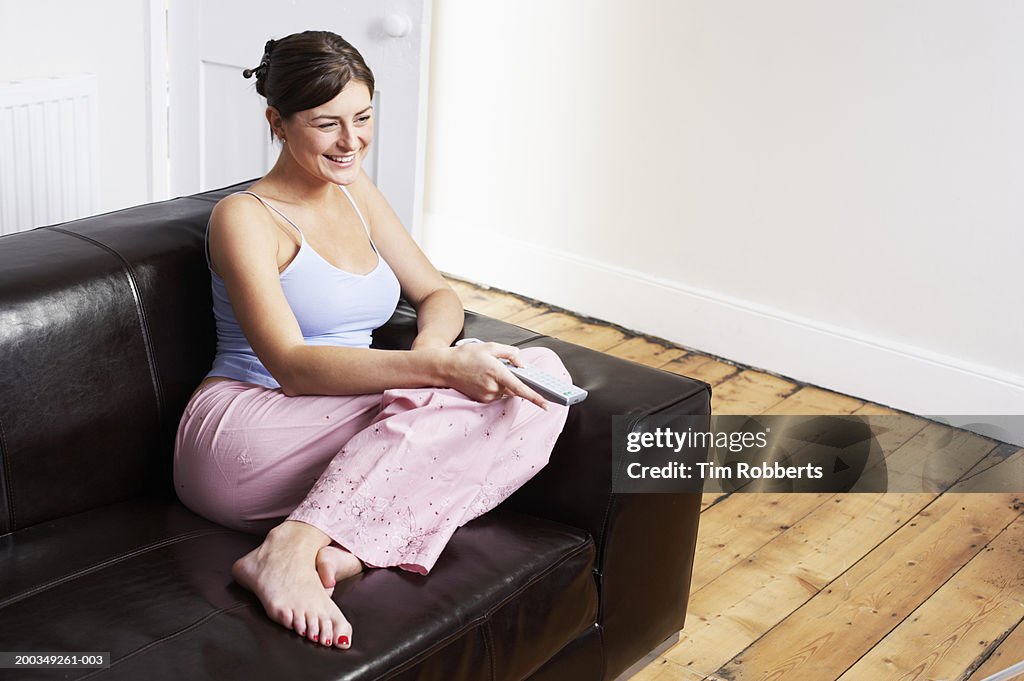 Young woman on sofa using television remote control