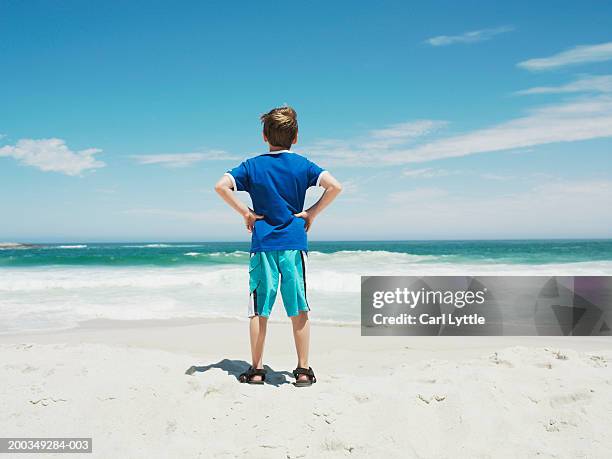 boy (9-11) standing on beach facing ocean, hands on hips, rear view - shorts ストックフォトと画像