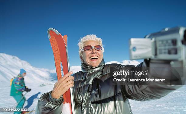 senior woman with skis smiling into video camera - senior winter sport stock pictures, royalty-free photos & images