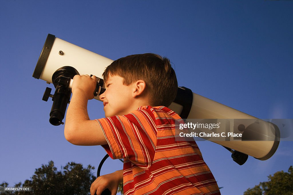 Boy (6-8) looking through telescope, close-up, side view, dusk
