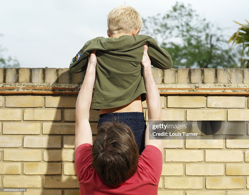 Man helping boy (7-9) over brick wall, rear view