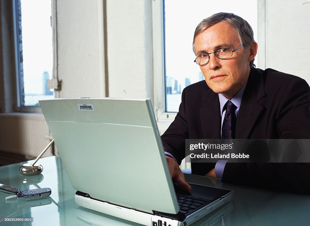 Mature businessman at desk with laptop, portrait