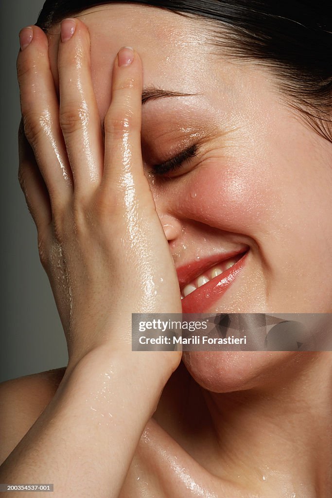 Young woman covering wet face with hand, smiling, close-up