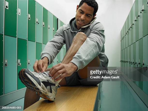 man sitting on bench in locker room tying laces and using mobile phone - green pants fotografías e imágenes de stock