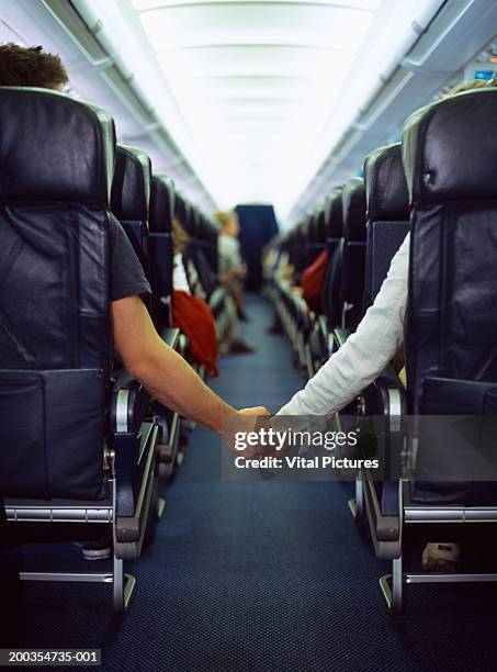 couple holding hands across aisle of passenger aeroplane, rear view - aisle seat airline stock-fotos und bilder