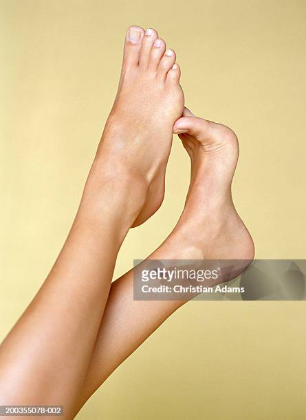 young woman rubbing bottom of foot with toes of other foot, close-up - adult woman legs close up stock-fotos und bilder