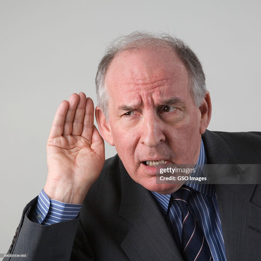 Senior businessman listening with hand cupped to ear, close-up