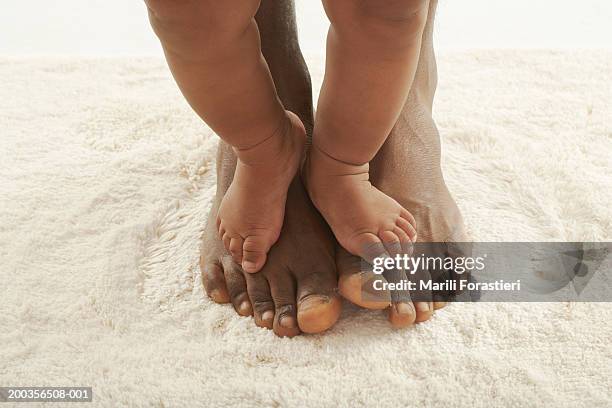 baby girl (6-9 months) standing on man's feet, low section - black men feet stock-fotos und bilder