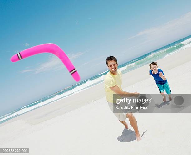 father and son (9-11) playing with boomerang on beach, smiling - boomerang stock pictures, royalty-free photos & images