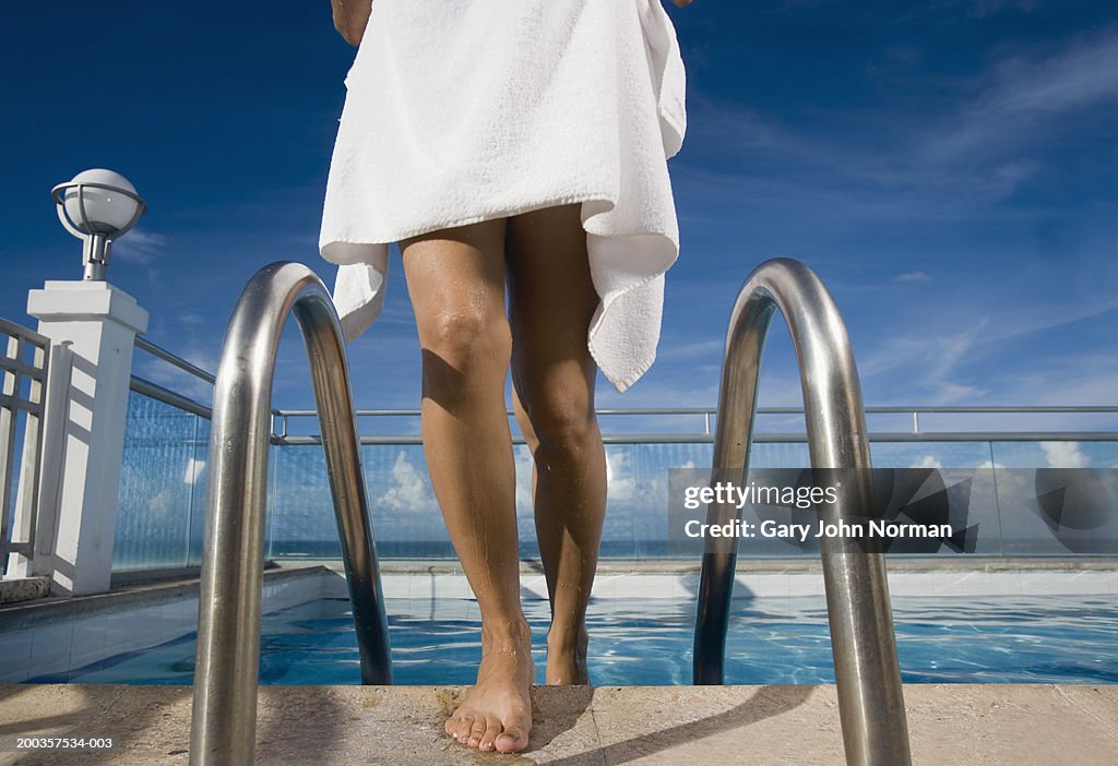 Woman climbing out of swimming pool, low section