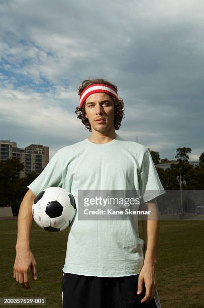 young man standing holding football, portrait - headband stock pictures, royalty-free photos & images