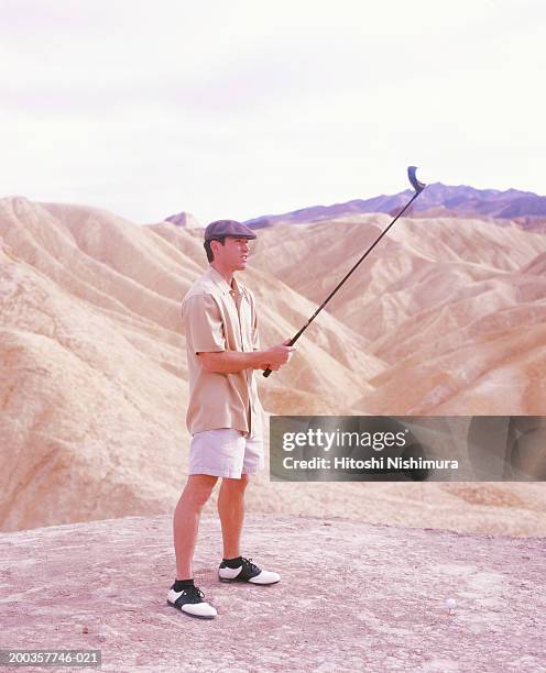 young man holding up golf club in rocky mountains - short sleeved stockfoto's en -beelden