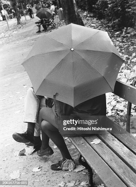 couple under umbrella sitting on bench, outdoors (b&w) - parkbänk bildbanksfoton och bilder