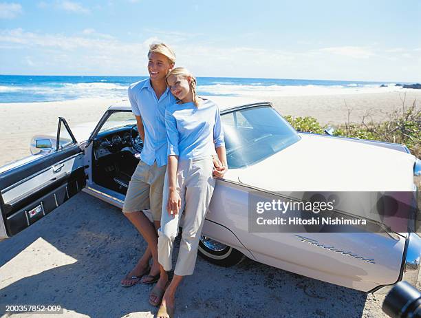 young couple leaning against car on beach - driving barefoot stock pictures, royalty-free photos & images