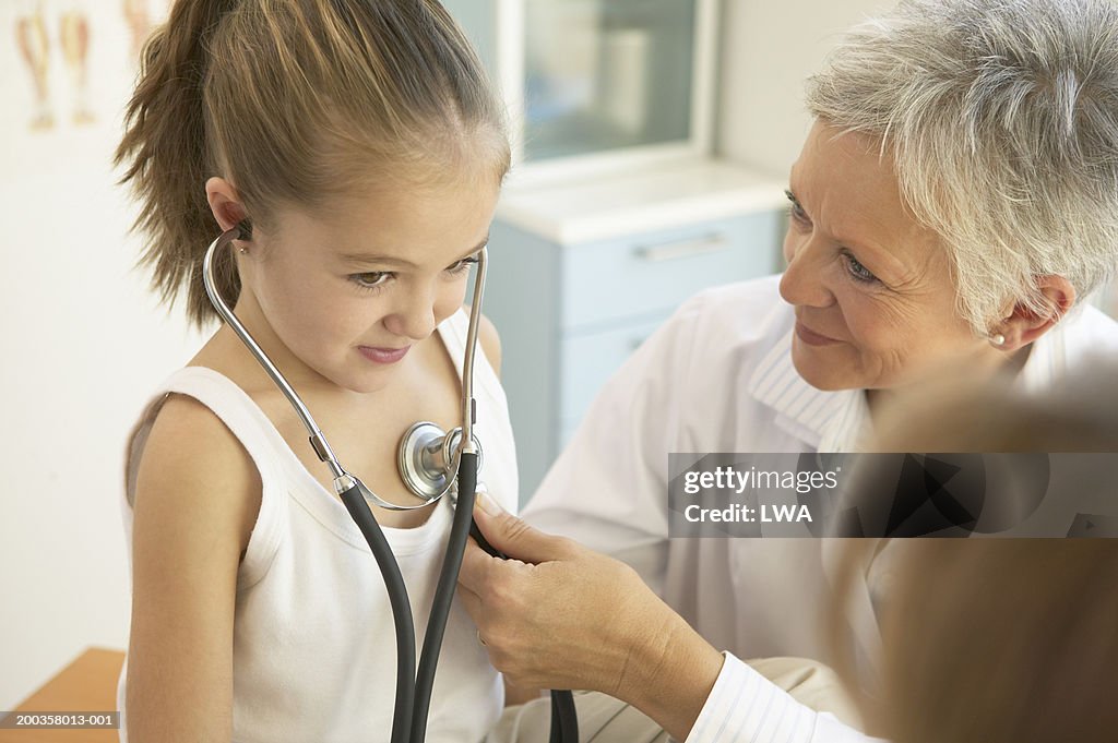 Mature female doctor examining girl (7-9), mother watching