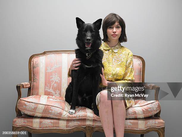 young woman and dog sitting side by side on love seat, portrait - tweezits bankje stockfoto's en -beelden