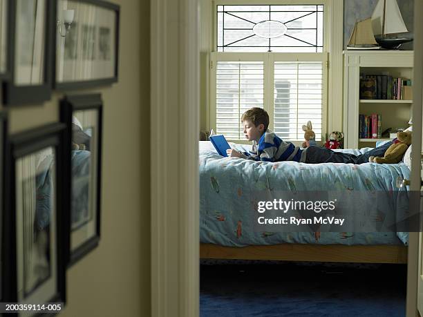 boy (7-9) reading book on bed, view from hallway - child's bedroom stockfoto's en -beelden