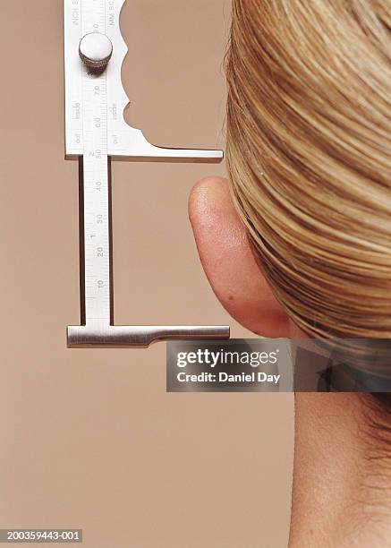 young woman having ear measured with calipers, close-up, rear view - ear close up women stock-fotos und bilder