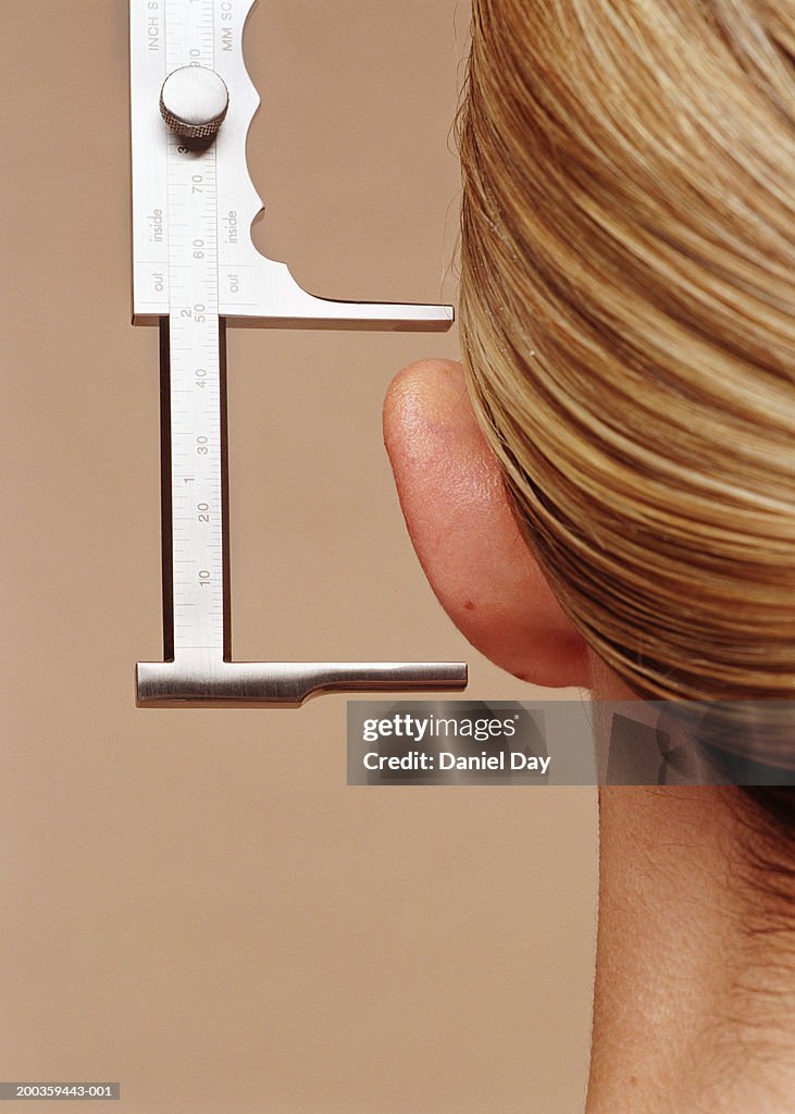 Young woman having ear measured with calipers, close-up, rear view