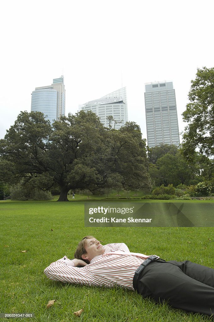 Businessman lying on back in park with hands behind head, eyes closed